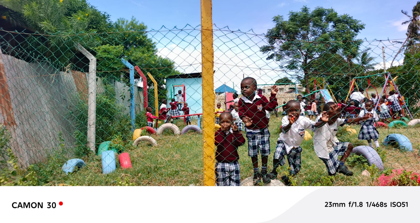 Kindergarten pupils playing near the playground fence with tire swings visible