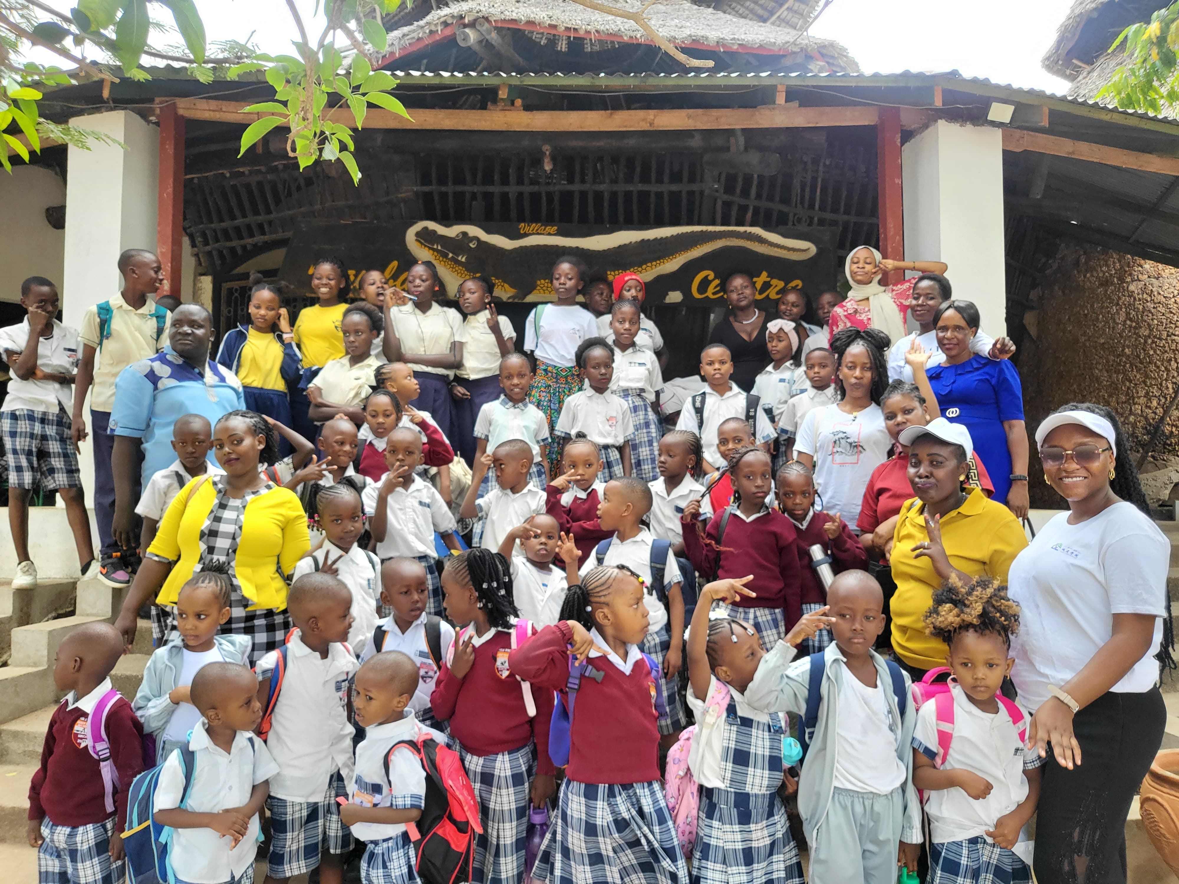 Full class and staff group photo at the Mamba Village entrance, alternate framing